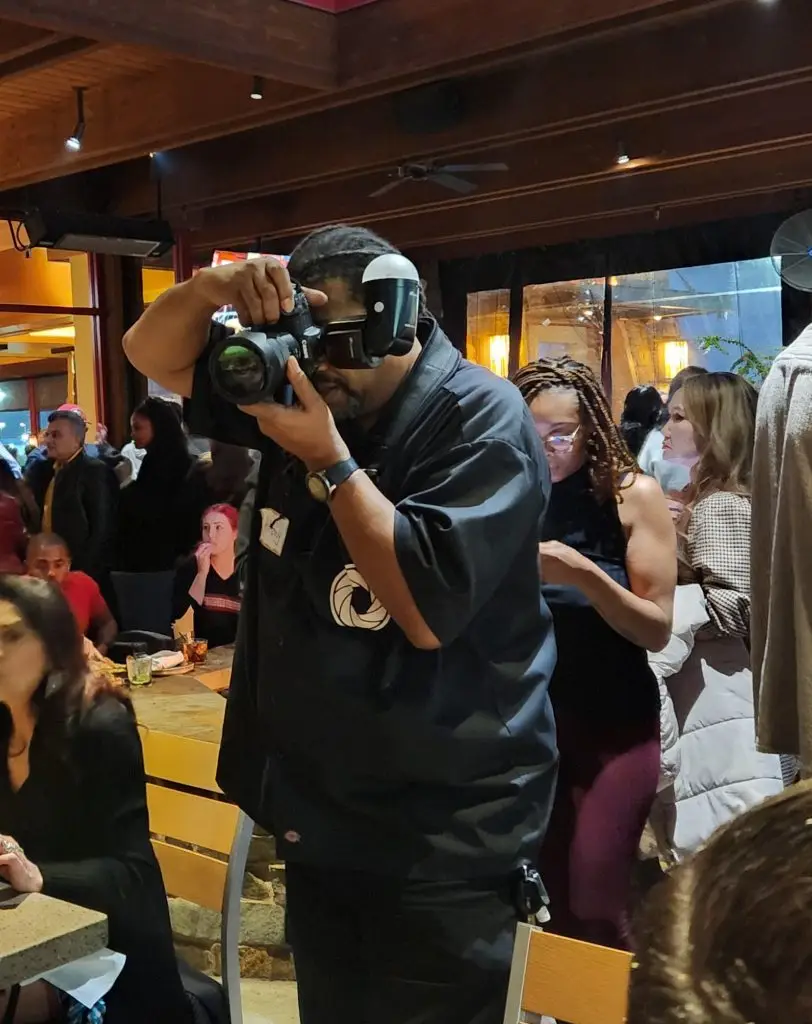 A photographer using a camera with a large lens at a crowded event, focusing on a subject.