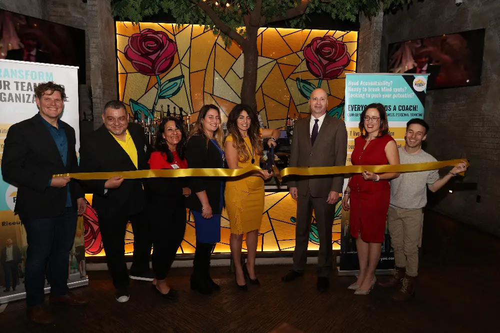 Group of individuals participating in a ribbon cutting ceremony with a large gold ribbon.