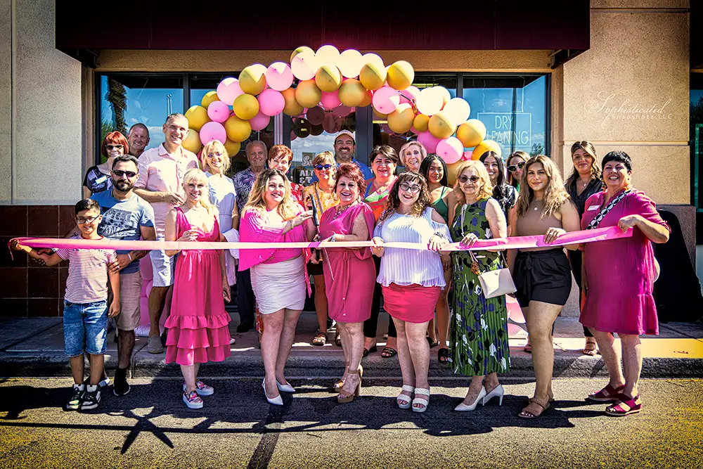 Group of people posing for a photo during a ribbon cutting ceremony with balloons in the background.