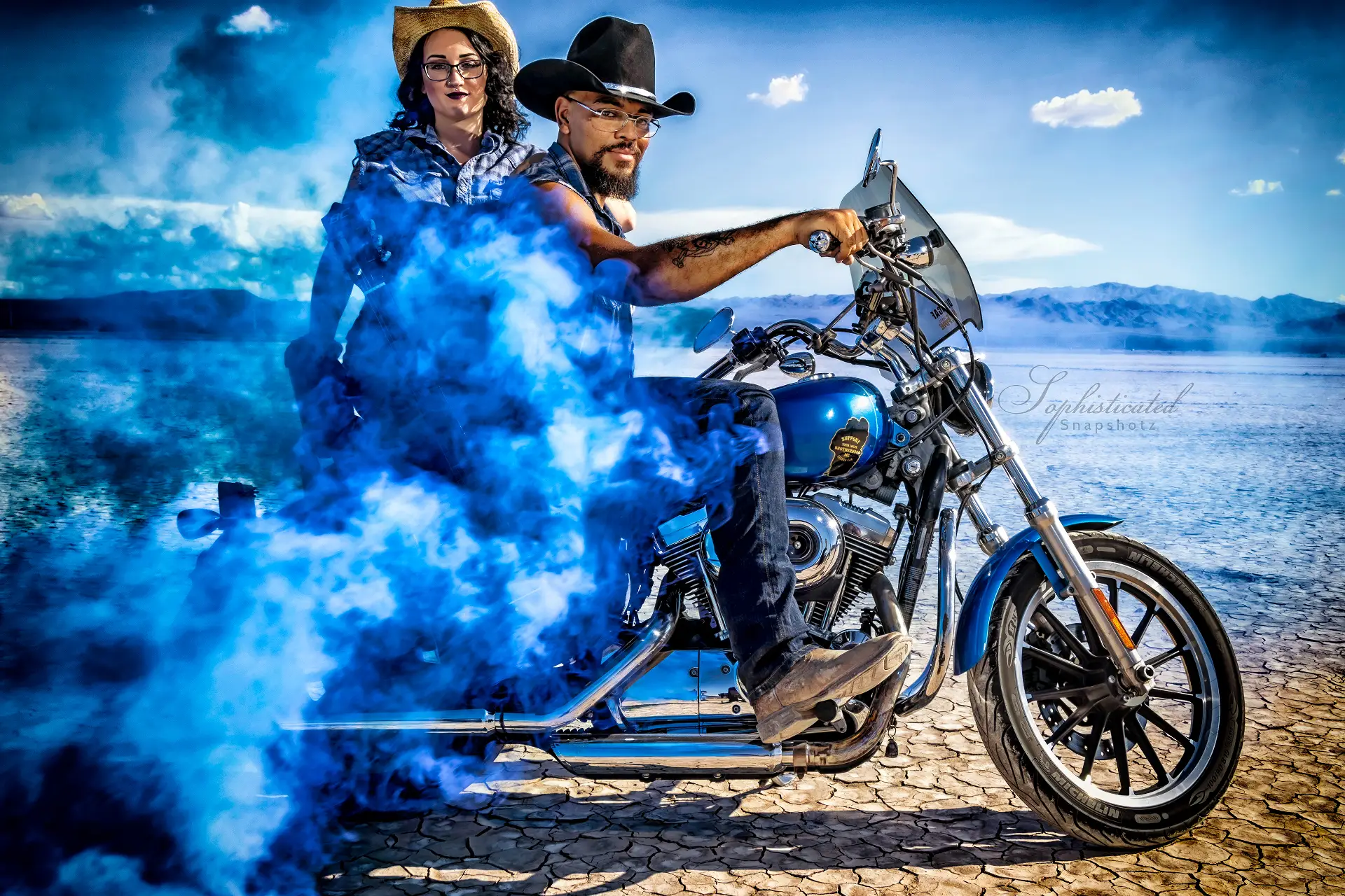A man wearing a cowboy hat rides a motorcycle with a woman behind him, surrounded by blue smoke.