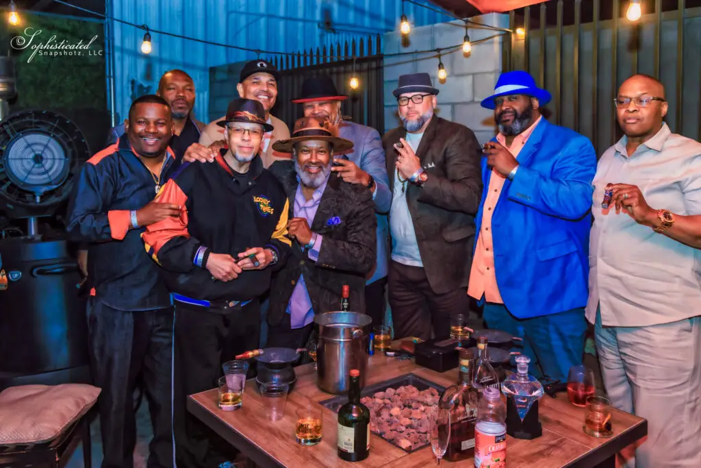 A group of men posing together with drinks in a social setting, smiling and interacting.