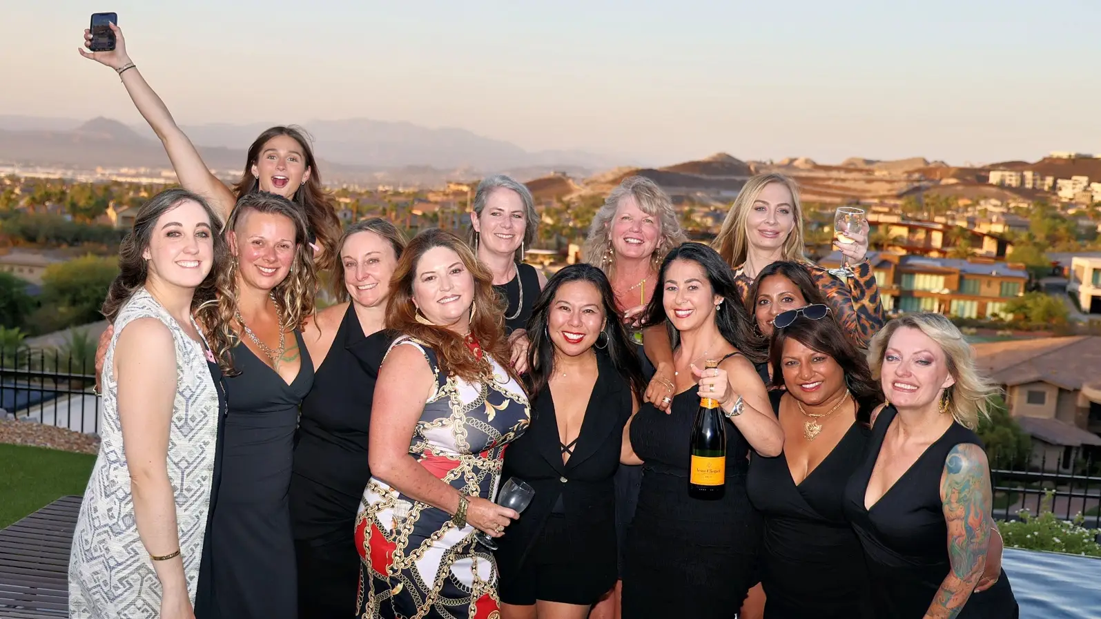 A group of women posing together outdoors, some holding drinks and smiling at the camera.