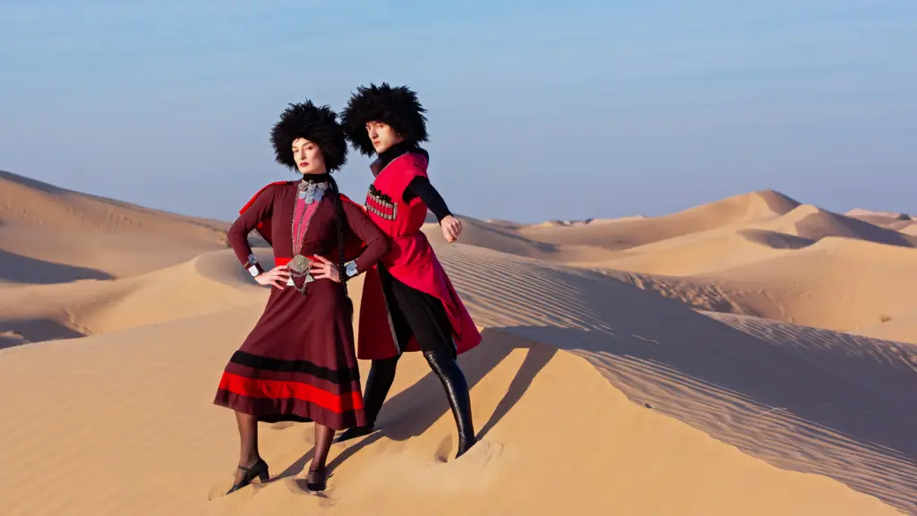 Two models posing in the desert wearing distinct fashion outfits with dramatic hairstyles.